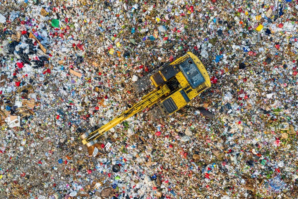 Aerial shot of a landfill with a yellow excavator in South Tangerang, Indonesia.